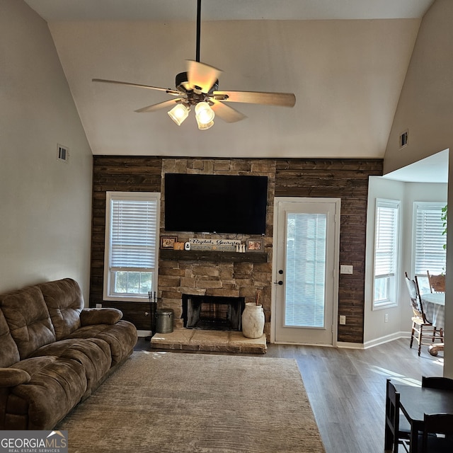 living room with a wealth of natural light, visible vents, a stone fireplace, and wood finished floors