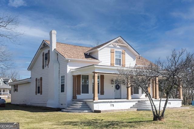 view of front of property with a shingled roof, a front yard, covered porch, and a chimney