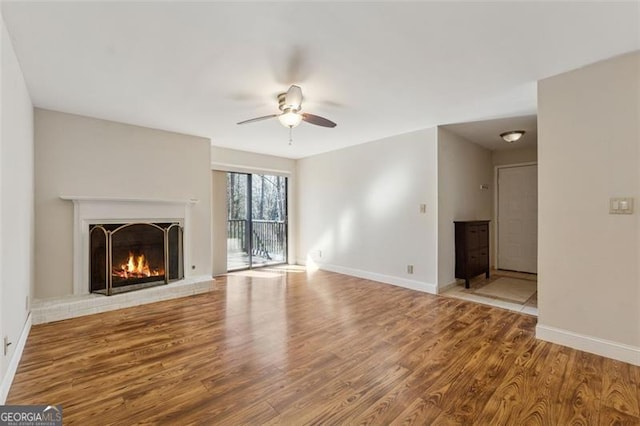 unfurnished living room featuring ceiling fan, a fireplace, baseboards, and wood finished floors