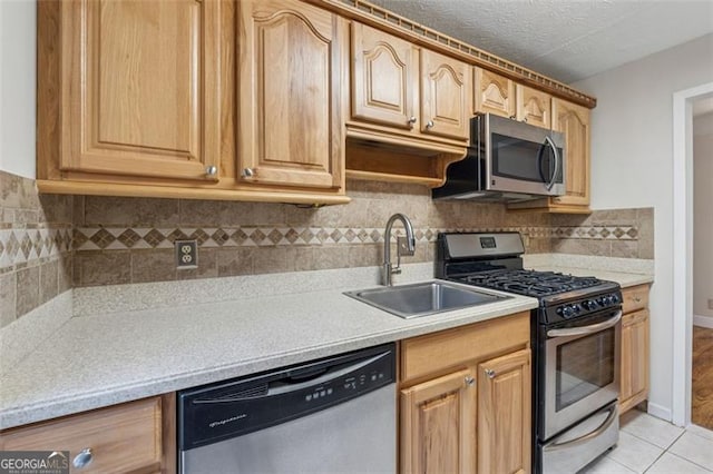 kitchen with light tile patterned floors, appliances with stainless steel finishes, light countertops, a textured ceiling, and a sink