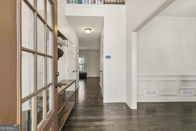 foyer entrance featuring dark wood-type flooring, a decorative wall, baseboards, and visible vents