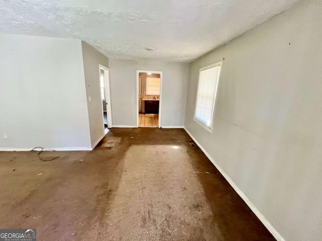 unfurnished living room with a textured ceiling and baseboards