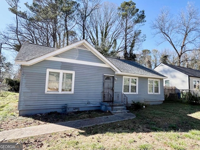 ranch-style house with a shingled roof, crawl space, fence, and a front lawn