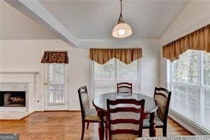 dining space with a healthy amount of sunlight, a fireplace, lofted ceiling with beams, and wood finished floors