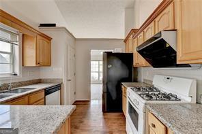 kitchen with light stone counters, a sink, white gas range oven, freestanding refrigerator, and dishwasher