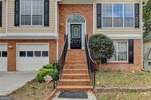 view of exterior entry featuring a garage, brick siding, and driveway