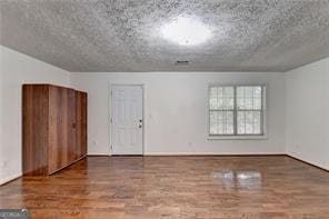 unfurnished room with a textured ceiling and wood finished floors