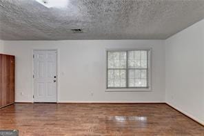 unfurnished room with visible vents, a textured ceiling, baseboards, and wood finished floors