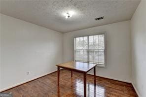 unfurnished office with visible vents, a textured ceiling, baseboards, and wood finished floors