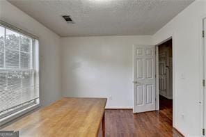 unfurnished office featuring visible vents, a textured ceiling, and wood finished floors