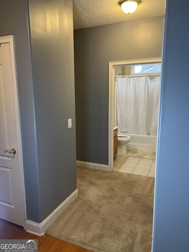 interior space with a textured ceiling, tile patterned flooring, toilet, baseboards, and shower / bath combo