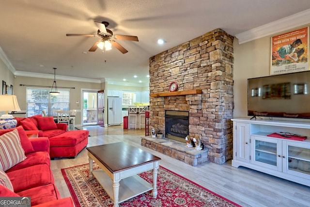 living area with ornamental molding, a ceiling fan, a stone fireplace, and wood finished floors