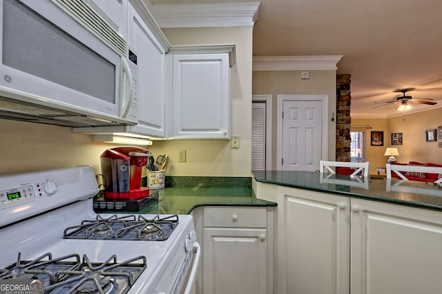 kitchen with ornamental molding, white appliances, dark countertops, and white cabinets