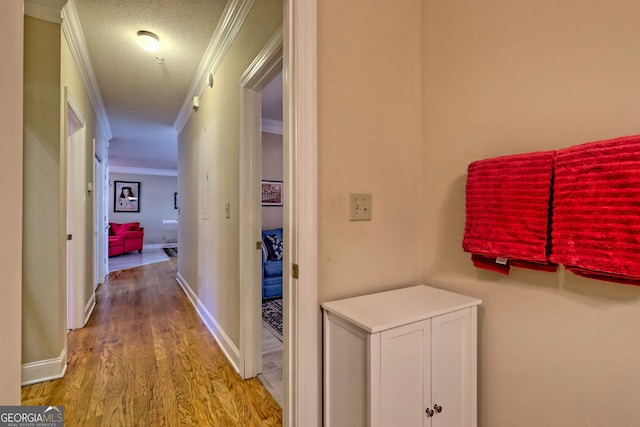 corridor with ornamental molding, a textured ceiling, baseboards, and wood finished floors