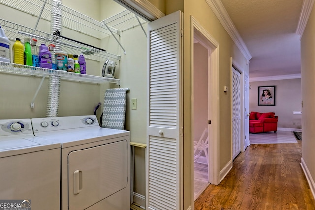 clothes washing area with washing machine and dryer, laundry area, wood finished floors, baseboards, and crown molding