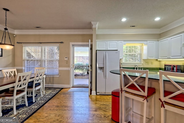 kitchen with crown molding, hanging light fixtures, light wood-style flooring, white cabinets, and white fridge with ice dispenser