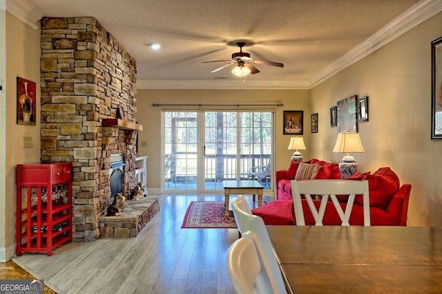 interior space with ceiling fan, a fireplace, wood finished floors, baseboards, and crown molding