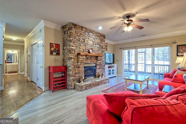 living area featuring ornamental molding, a stone fireplace, baseboards, and wood finished floors