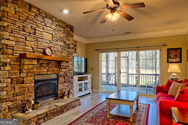 living area featuring a stone fireplace, wood finished floors, a ceiling fan, visible vents, and crown molding