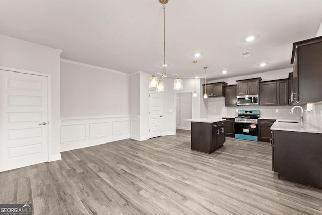 kitchen with light wood finished floors, stainless steel appliances, a sink, dark brown cabinetry, and a kitchen island