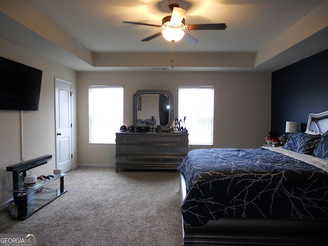 carpeted bedroom featuring baseboards, a tray ceiling, and ceiling fan