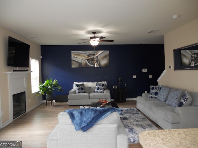 living area with light wood-style floors, ceiling fan, a fireplace, and baseboards