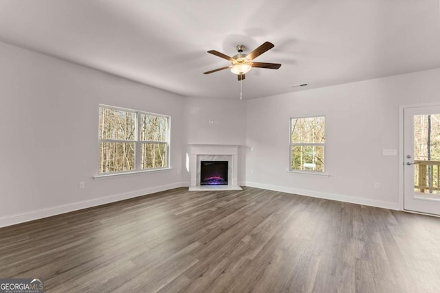 unfurnished living room with dark wood-style flooring, plenty of natural light, a fireplace, and baseboards