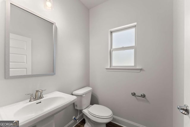 half bath featuring wood finished floors, a sink, toilet, and baseboards