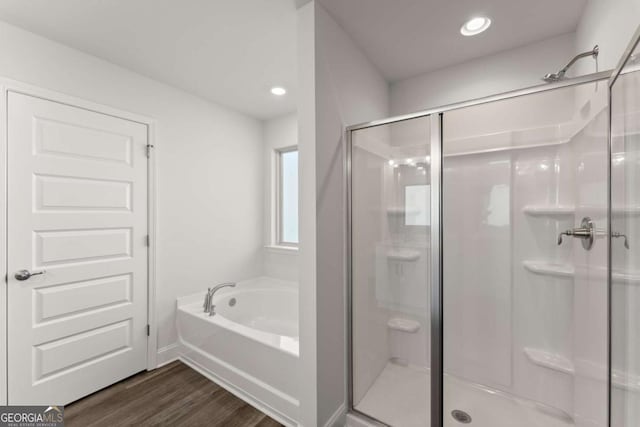 bathroom with wood finished floors, a stall shower, a garden tub, and recessed lighting