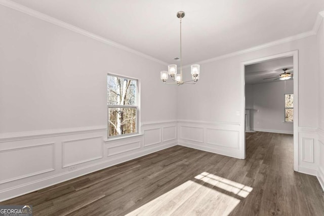 unfurnished dining area featuring dark wood-style floors, wainscoting, ceiling fan with notable chandelier, and crown molding