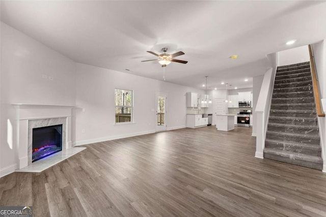 unfurnished living room with ceiling fan, stairs, dark wood finished floors, and a premium fireplace