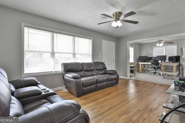 living room featuring ceiling fan, a textured ceiling, baseboards, and wood finished floors