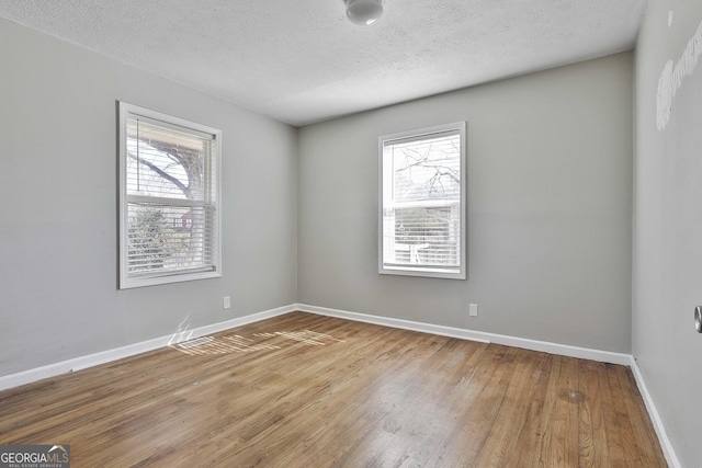 empty room featuring a wealth of natural light, light wood-style flooring, baseboards, and a textured ceiling