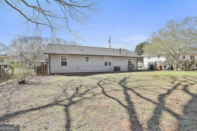 rear view of house featuring fence, central AC unit, and a yard