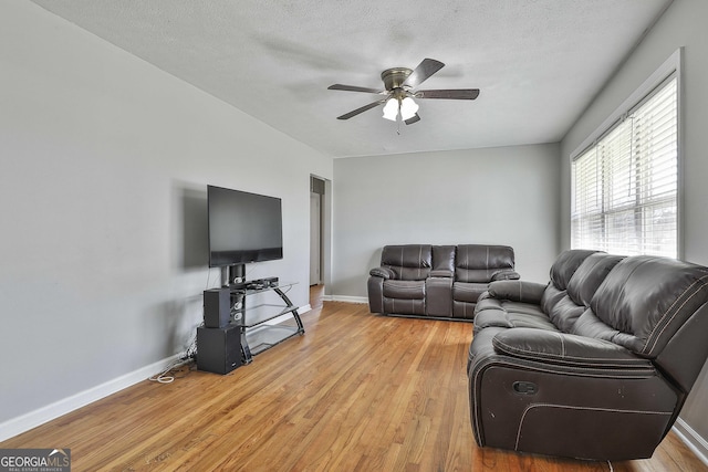 living room with light wood-style floors, baseboards, a ceiling fan, and a textured ceiling