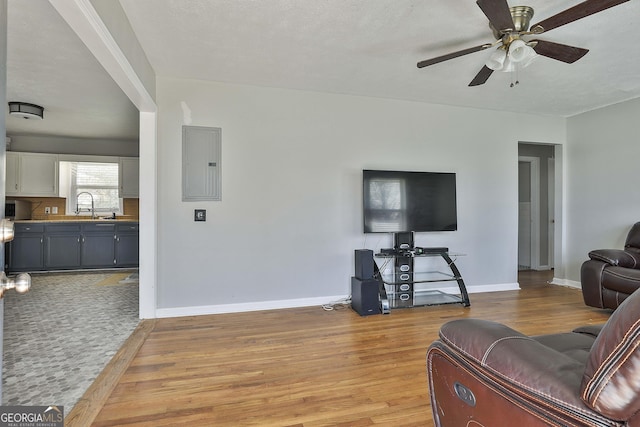 living room featuring light wood-type flooring, electric panel, baseboards, and a ceiling fan