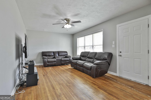 living area featuring a textured ceiling, light wood-type flooring, and baseboards