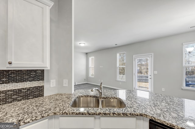 kitchen featuring stone countertops, white cabinetry, backsplash, and a sink