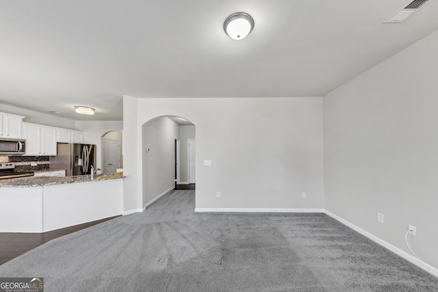 kitchen featuring visible vents, arched walkways, dark stone countertops, stainless steel appliances, and white cabinetry