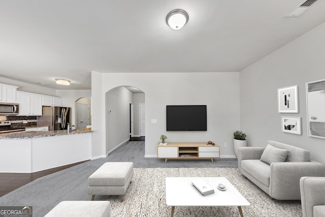 carpeted living room with visible vents, arched walkways, and baseboards