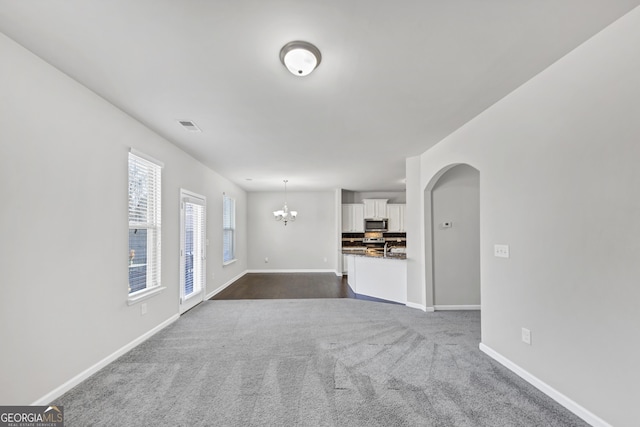 unfurnished living room featuring arched walkways, baseboards, visible vents, and an inviting chandelier