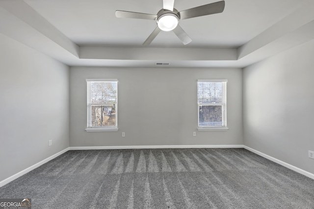 spare room featuring dark colored carpet, a raised ceiling, visible vents, and baseboards