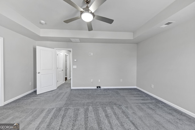 unfurnished bedroom with visible vents, a tray ceiling, baseboards, and carpet flooring