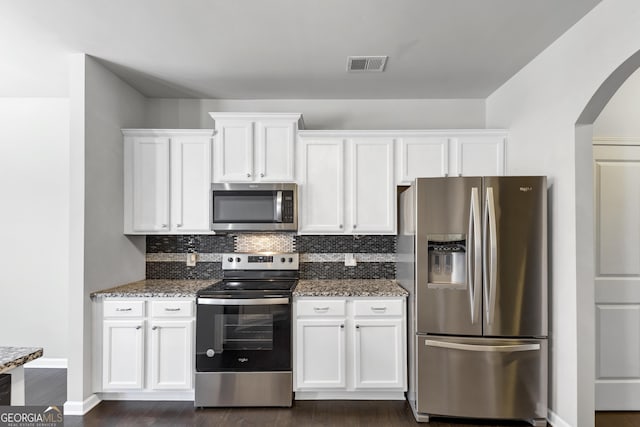 kitchen with visible vents, decorative backsplash, dark stone countertops, stainless steel appliances, and white cabinetry