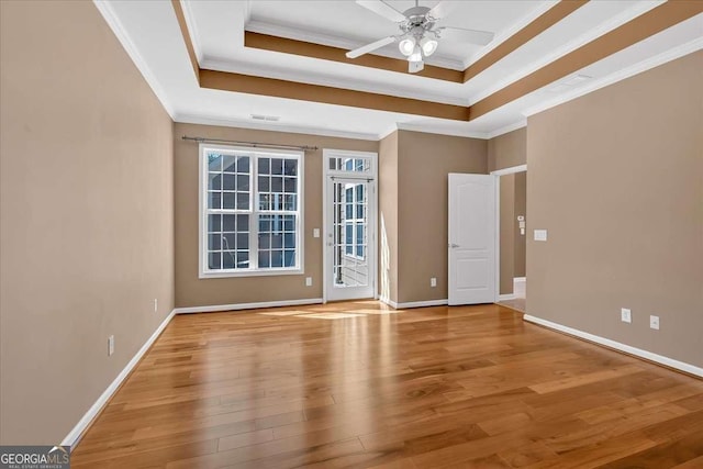 unfurnished room featuring crown molding, a tray ceiling, wood finished floors, and baseboards