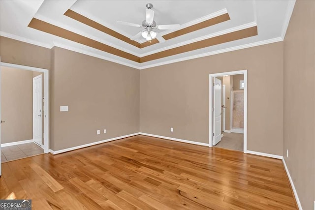 spare room with baseboards, ceiling fan, a tray ceiling, crown molding, and light wood-style floors