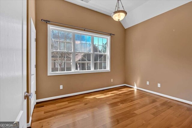 spare room with vaulted ceiling, wood finished floors, and baseboards