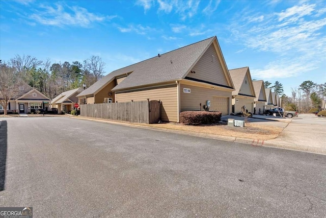 view of home's exterior with driveway, an attached garage, fence, and a residential view