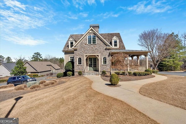 view of front of house with stone siding, a chimney, metal roof, a standing seam roof, and a porch