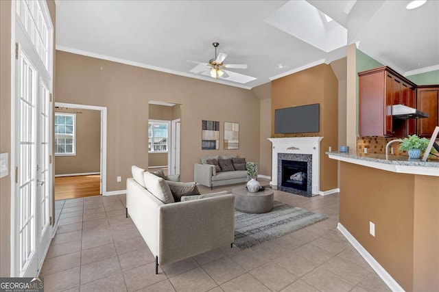 living room featuring a fireplace, light tile patterned floors, ornamental molding, a ceiling fan, and baseboards